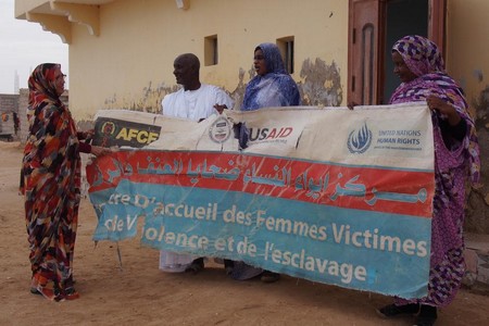 Aminetou Ely et des collaborateurs de l'Association des femmes chefs de famille, déployant à Dar Naïm une banderole du « Centre d’accueil des Femmes Victimes de Violence et de l’esclavage ». Novembre 2016. © 2016 Marie Foray